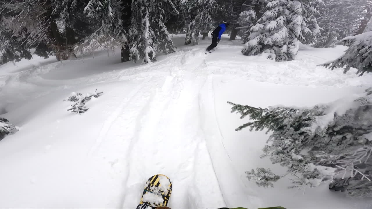 Snowboarder recording himself and his friend descending by the slope. Sportsman practicing in the beautiful snowy forest.