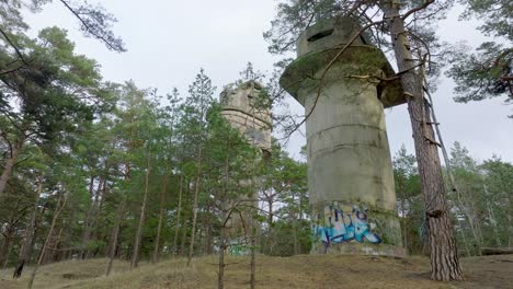 Establishing-aerial-view-of-old-Soviet-military-concrete-observation-watchtower,-pine-tree-forest,-Liepaja-,-military-heritage,-Nordic-woodland,-low-wide-drone-dolly-shot-moving-left