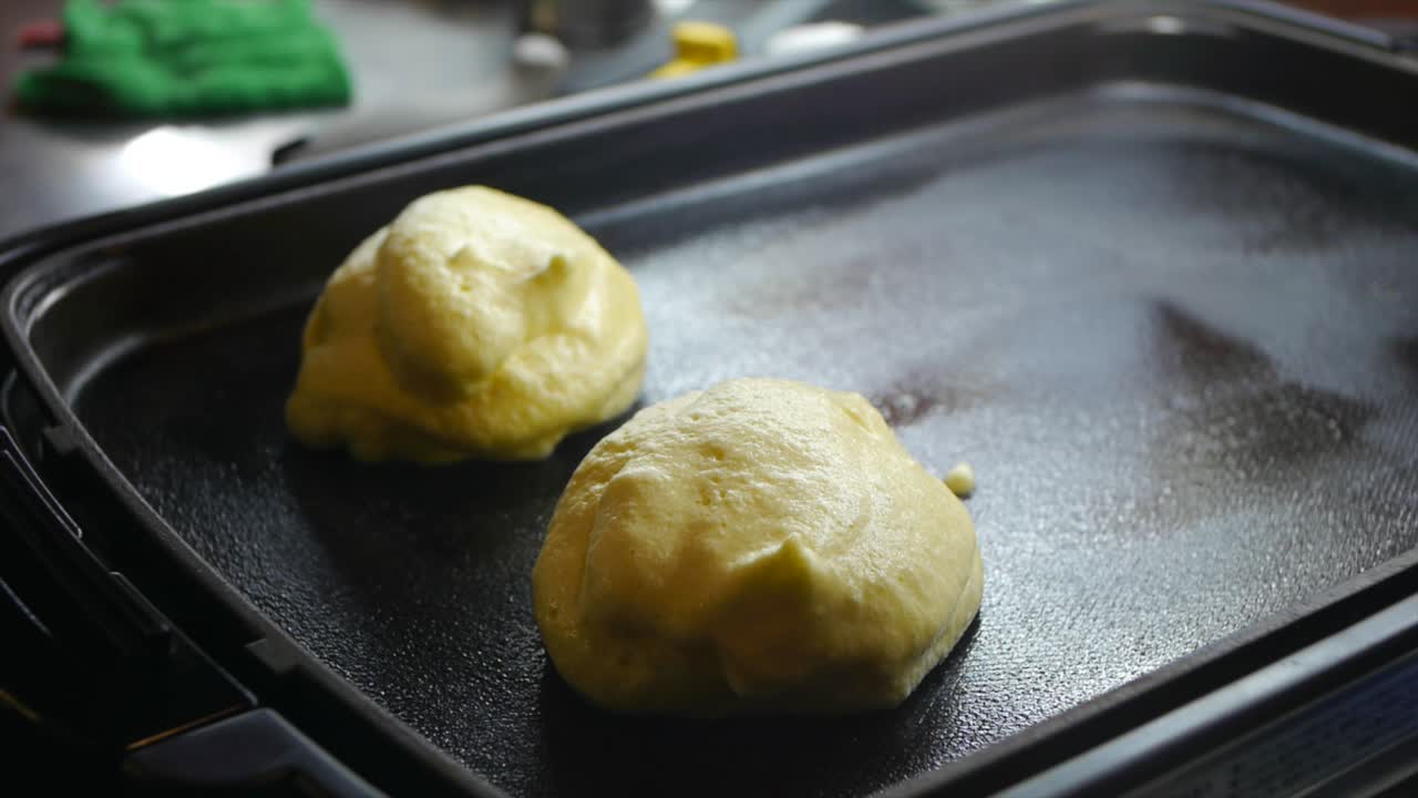 Impasto per pancake e waffle versato a cucchiaiate su una padella unta, filmato in primo piano.