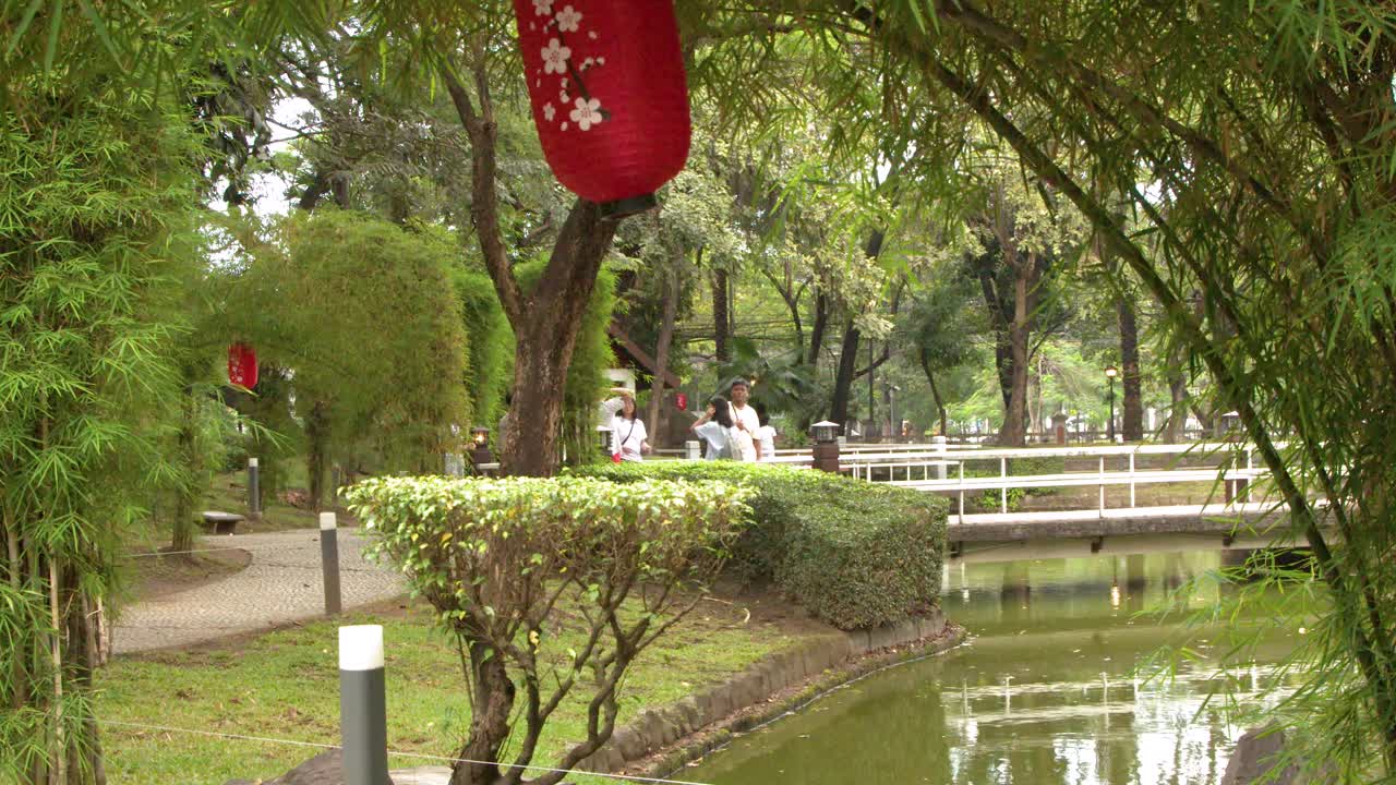 Một chiếc đèn lồng đỏ treo trên những cây tre nhìn ra ao và cầu ở Manila.