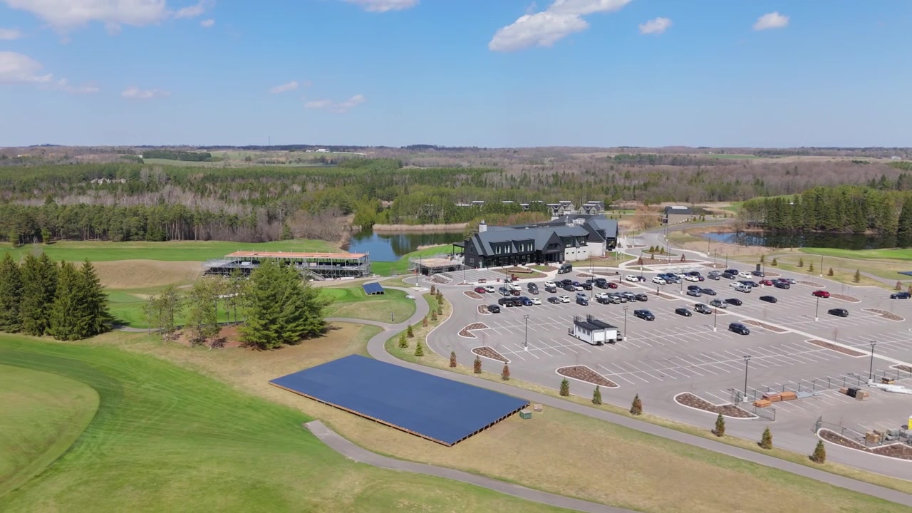 A golf clubhouse with a large parking area, surrounded by lush greenery and a serene landscape. Ideal for travel promotions and real estate marketing.