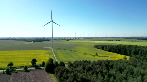 Panorama,-Turbina-Eólica-En-Un-Campo-De-Colza-Y-Automóviles-Circulando-Por-La-Carretera,-Fuentes-De-Energía-Renovables