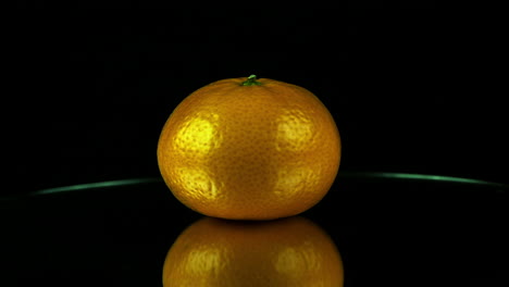 Low-angle-view:-Clementine-orange-rotates-on-mirror-in-dark-studio