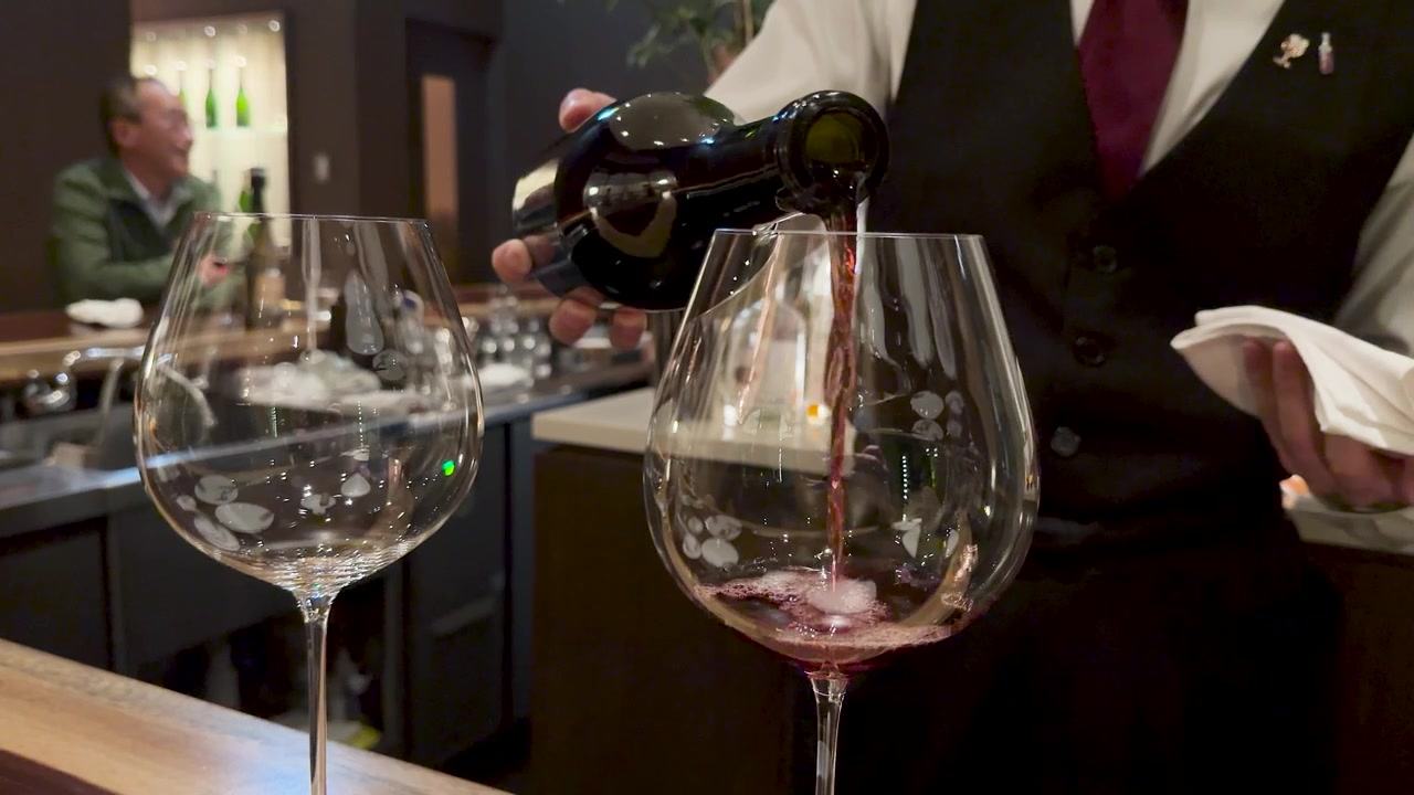 Un sommelier professionista versa vino rosso in un grande calice di cristallo al bar di un ristorante.