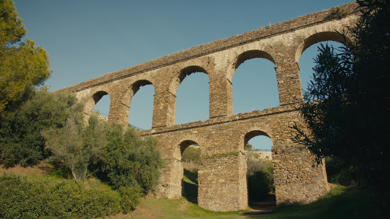 Antico acquedotto in pietra in un paesaggio naturale filmato in time-lapse, con la luce del sole che cambia e gli arbusti che ondeggiano dolcemente al vento