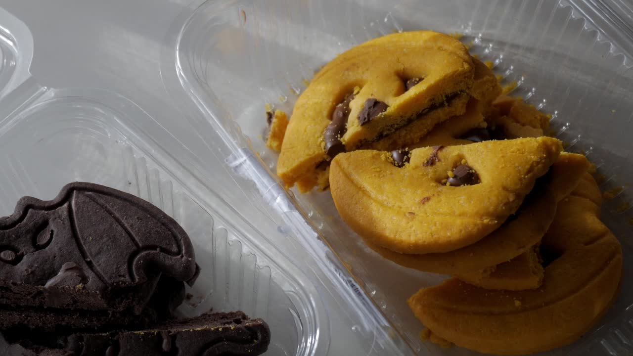 Close-up of yellow pumpkin-shaped cookies with chocolate chips inside a transparent plastic container under daylight