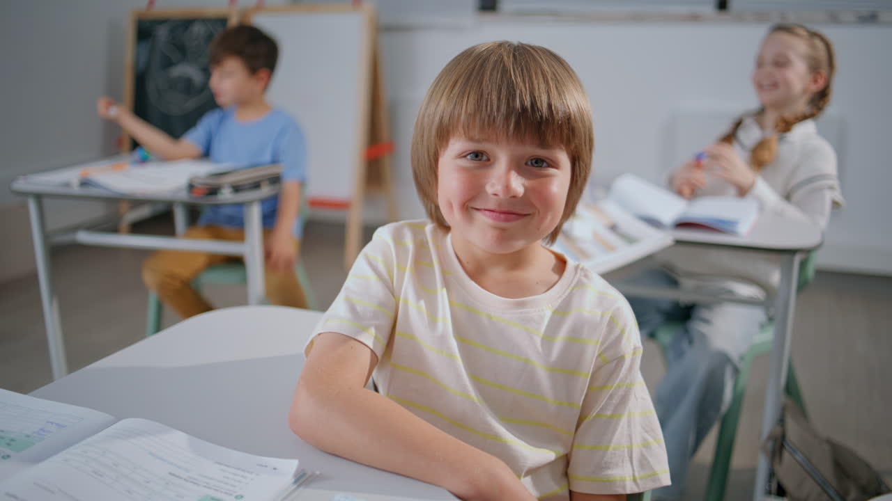 Ritratto di un allegro alunno che guarda la telecamera a scuola. Bambino felice seduto in classe