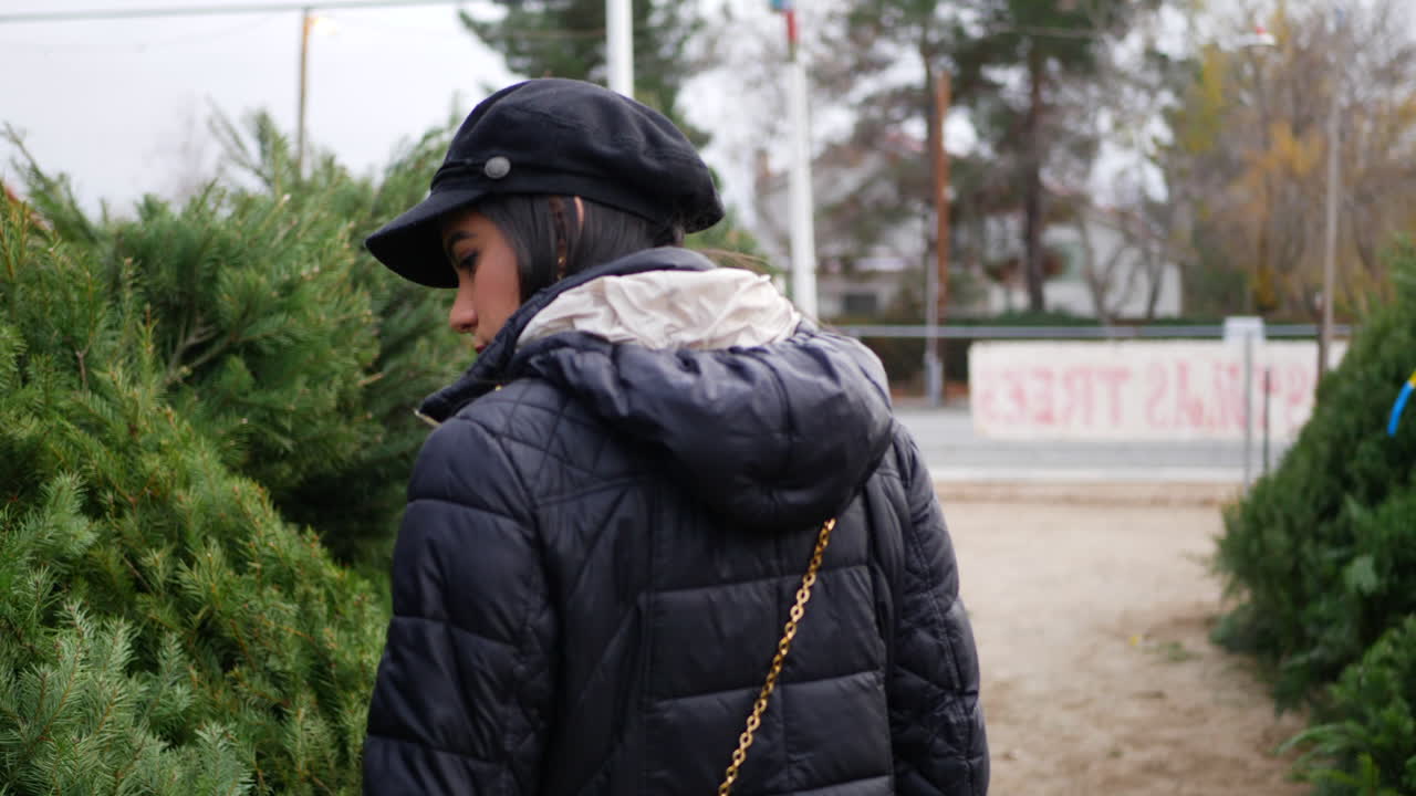 많은 종류의 축제 나무가 있는 제철 휴일 크리스마스 트리 장식을 쇼핑하는 히스패닉 여성