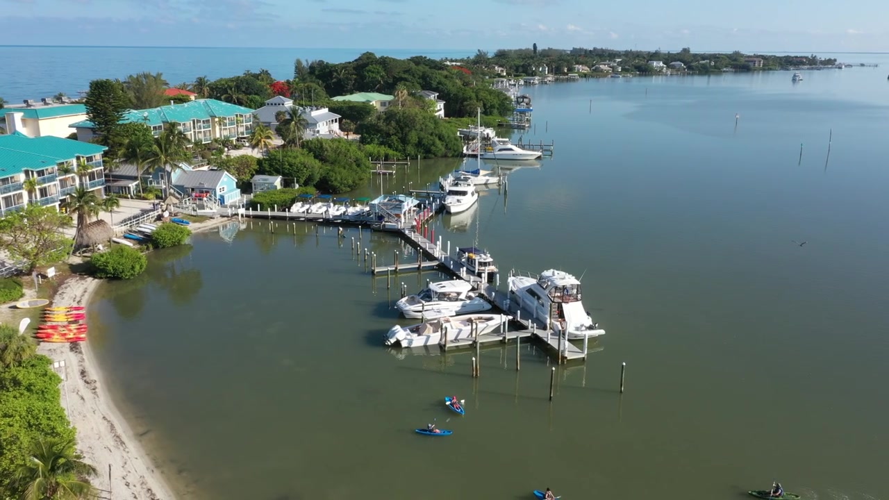 Letecký pohled dronem na Tween Waters Inn a Marinu v Captivě na Floridě, se zelenými střechami budov, zakotvenými jachtami a klidným Rooseveltovým průlivem lemovaným zálivem.