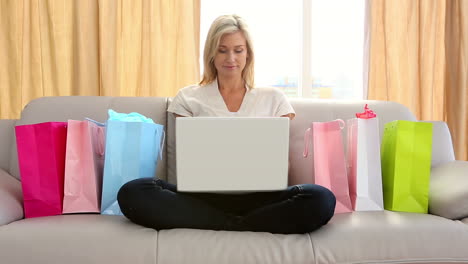 Pretty-blonde-sitting-on-couch-shopping-online-surrounded-by-bags