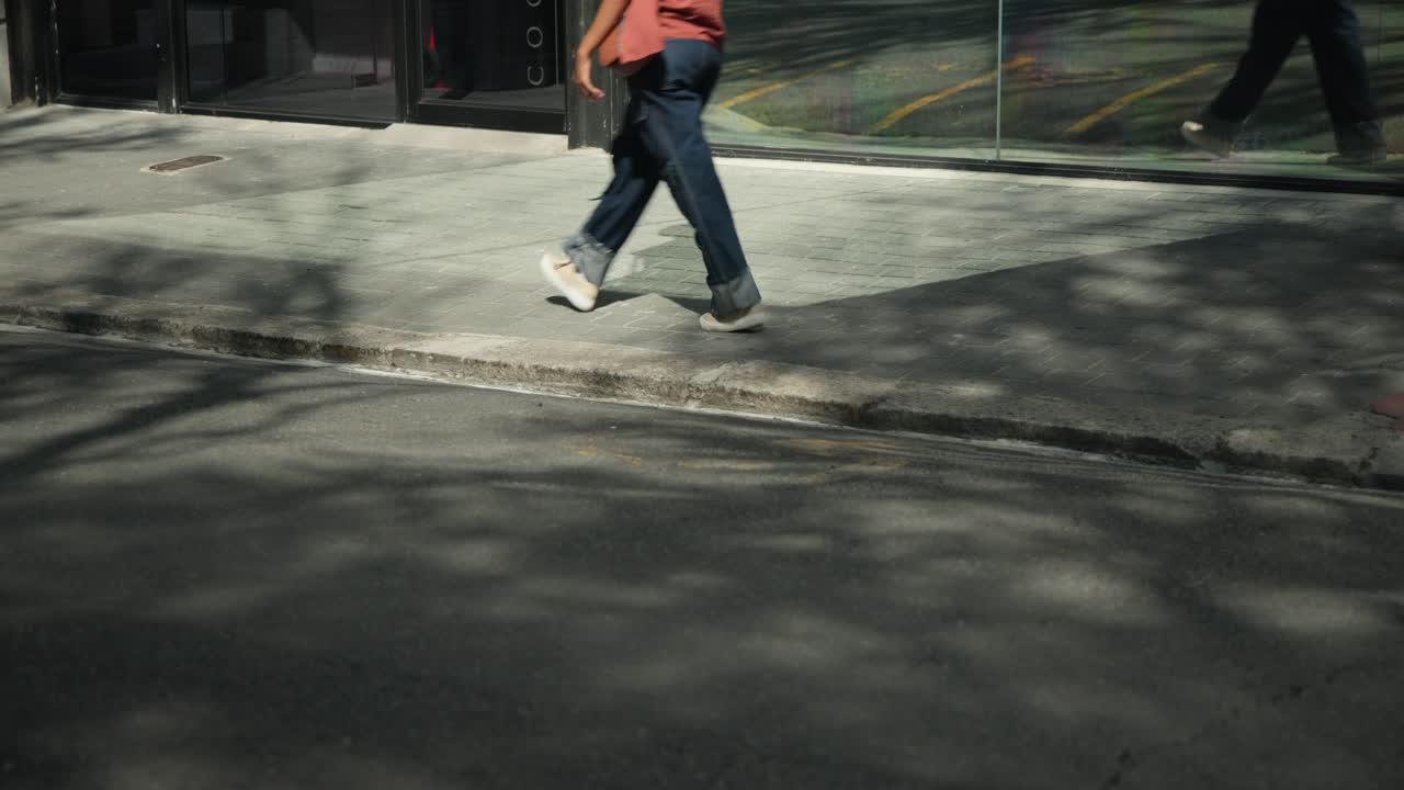 Diverse pedestrians entering from left, walking across sidewalk by reflective glass, heading onward