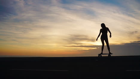 against the mountainous backdrop, a beautiful skateboarder in shorts rides her board along a mountain road at sunset in slow motion, offering a mesmerizing view