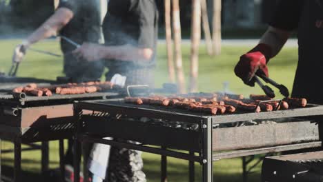 dos hombres hornean algunas carnes en rejillas muy brillantes y las giran