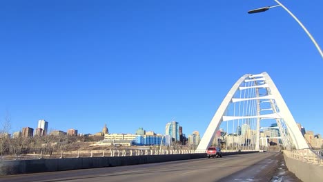 primer plano todoterreno rojo entrando en el moderno puente de arco atado walter dale blanco sobre el río saskatchewan del norte con una cresta en el horizonte de la legislatura la planta de energía junto a la junta de tesorería de alberta 2-2