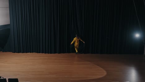woman in yellow dances expressively on dark stage alone