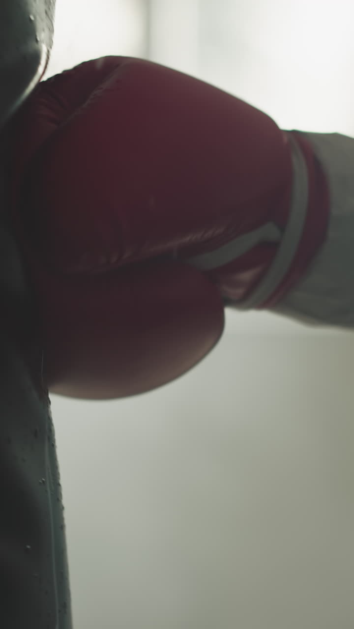 Strong man hand in fighting glove makes strike to fighting bag demonstrating strength. Improved stamina and physical health in equipped room for athletes