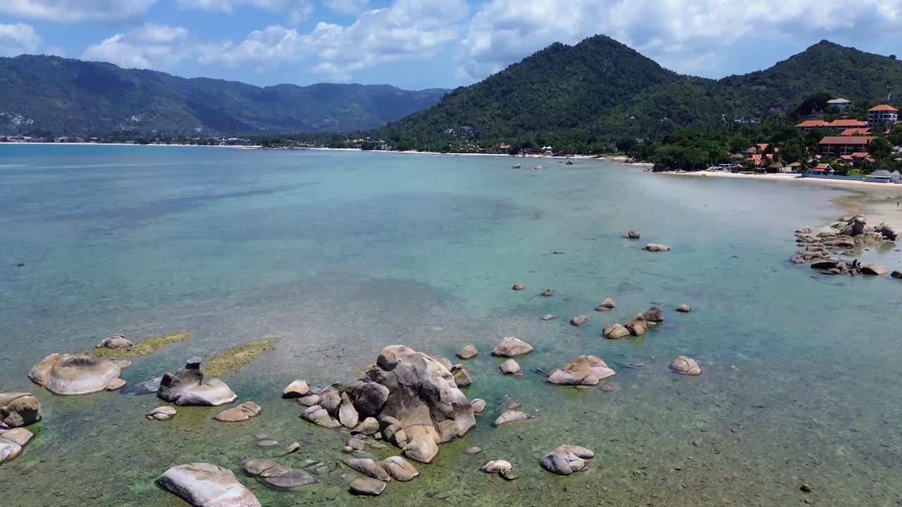 Aerial drone footage of Lamai Beach in Koh Samui, Thailand, featuring turquoise ocean, rocky shoreline, tropical island horizon, and scenic coastal landscape under clear tropical skies