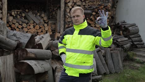 lumberjack in reflective jacket. man woodcutter show ok sign. sawn logs, firewood background