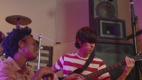 energetic boy playing guitar while girl with beer bottle listening to him during a rehearsal in recording studio