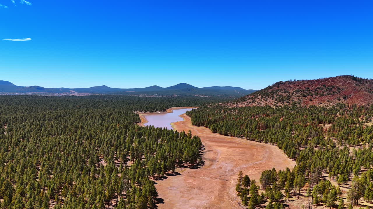 Flight over the bare land in the wood where the river flowed. Silhouette of mountain range against clear blue sky at backdrop. Scenery of Arizona, USA