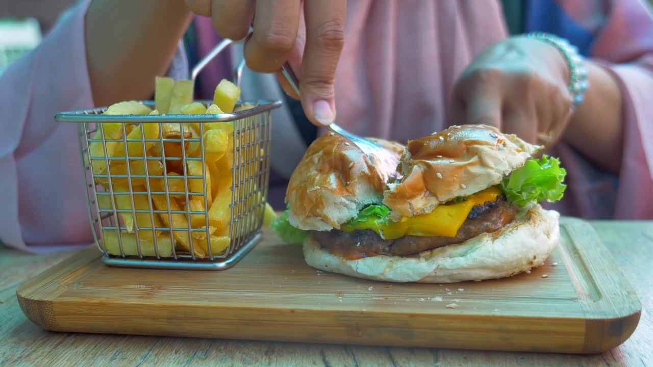 mujer comiendo una hamburguesa con queso y papas fritas