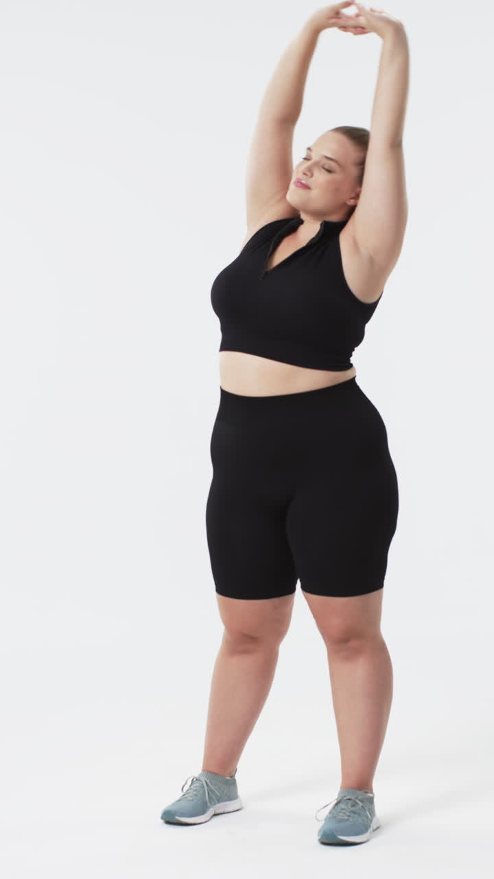 Video verticale: Donna curvy in abbigliamento sportivo che si allunga con le braccia alzate, promuovendo la body positivity.