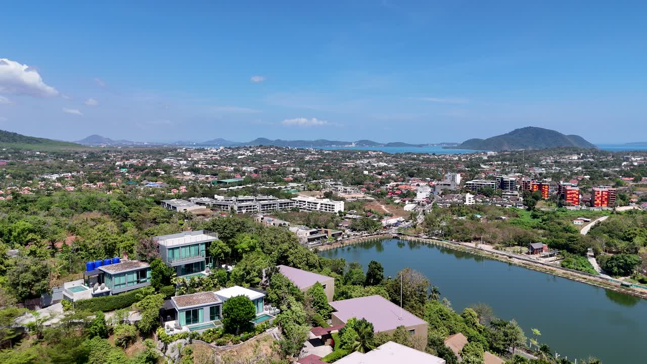 las imágenes de drones capturan una vista panorámica de la exuberante vegetación, los edificios y la costa de phuket bajo un cielo azul claro.