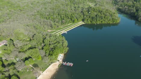 Antena-De-Una-Pequeña-Playa-De-Montaña-Con-Algunas-Personas-En-Un-Hermoso-Lago-Verde-Durante-Una-Calurosa-Y-Soleada-Tarde-De-Verano