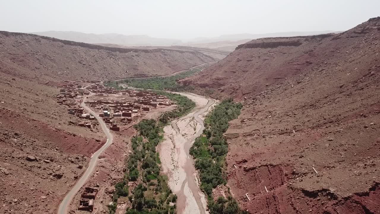 Vista drone di un canyon desertico con un fiume serpeggiante e vegetazione di oasi verde a Ouarzazate. Contrasto paesaggistico drammatico ideale per immagini di natura, ambiente e cinematografiche
