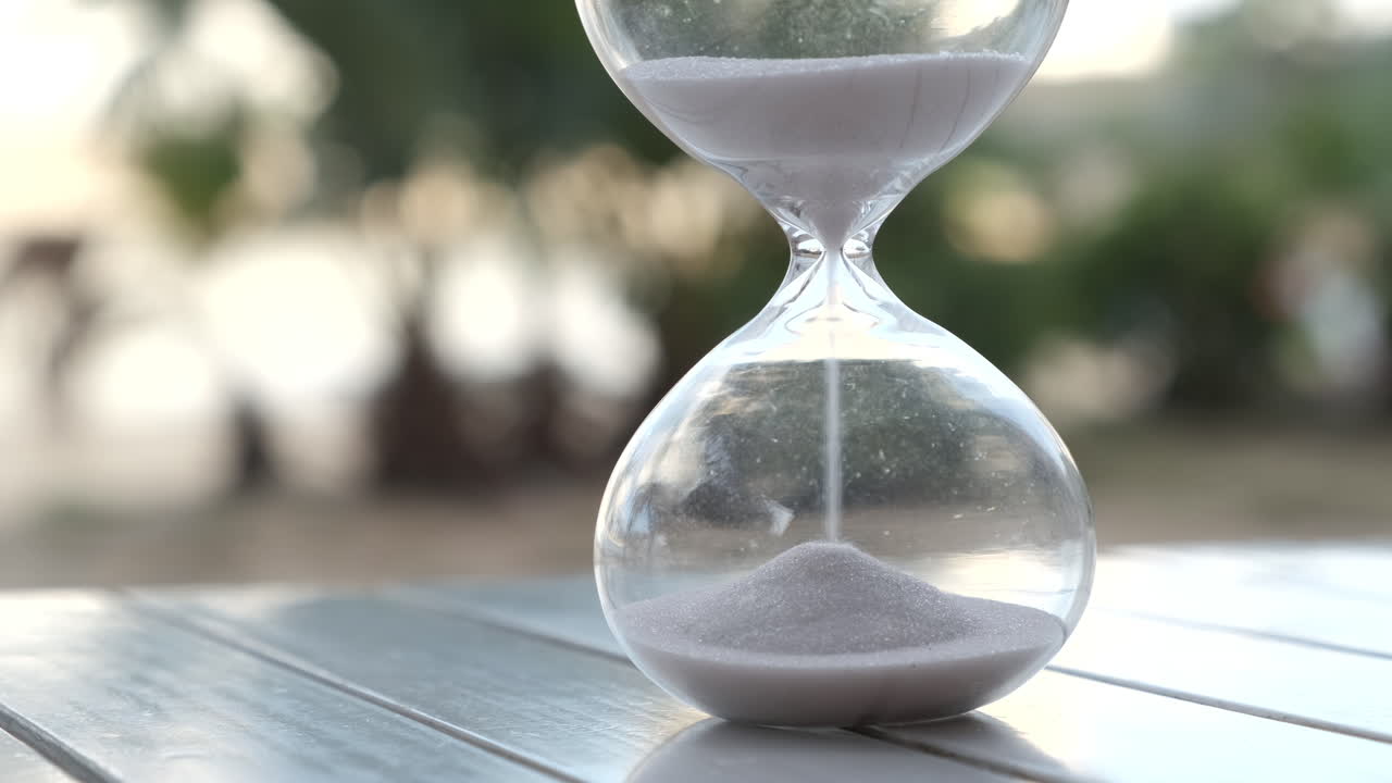 Hourglass as time passing on wooden table with bokeh background