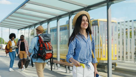 viajera caucásica con sombrero con mochila y maleta en la parada de autobús, luego saluda a un joven viajero