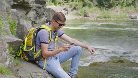 Eine-Person-Benutzt-Ein-Smartphone-Bei-Einer-Wanderung-Sitzt-An-Einem-Wunderschönen-Bergfluss