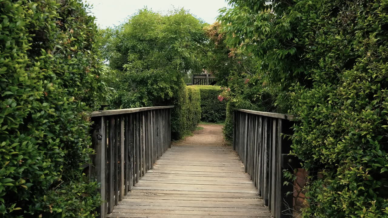 POV Of A Person Walking A Wooden Bridge To Hedge Maze