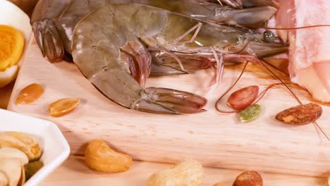 close-up of fresh shrimp, assorted nuts, and sliced meat on a wooden board.