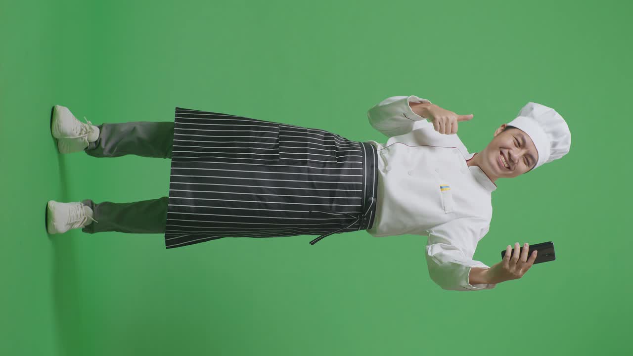 Full Body Of Asian Man Chef Using Smartphone Taking Picture While Standing In The Green Screen Background Studio