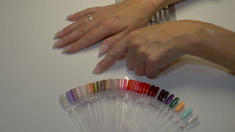 Close-up-shot-of-nervous-woman-choosing-color-of-nails-on-color-palette-and-taking-purple-color