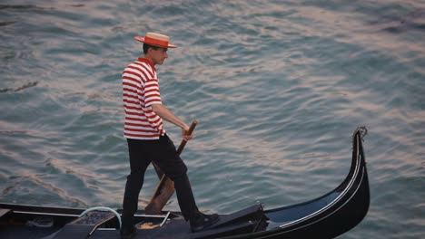 gondolier driving gondola, in venice canal, wearing red striped shirt and hat