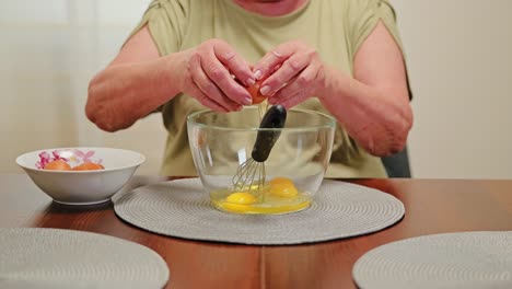 static shot of latvian grandma cracking eggs into bowl on wooden table, slow mo