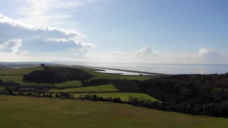 Aerial-shot-flying-over-fields-and-grass-with-a-beach-and-coast-in-the-background