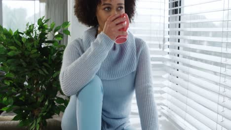 woman having a coffee sitting on window sill