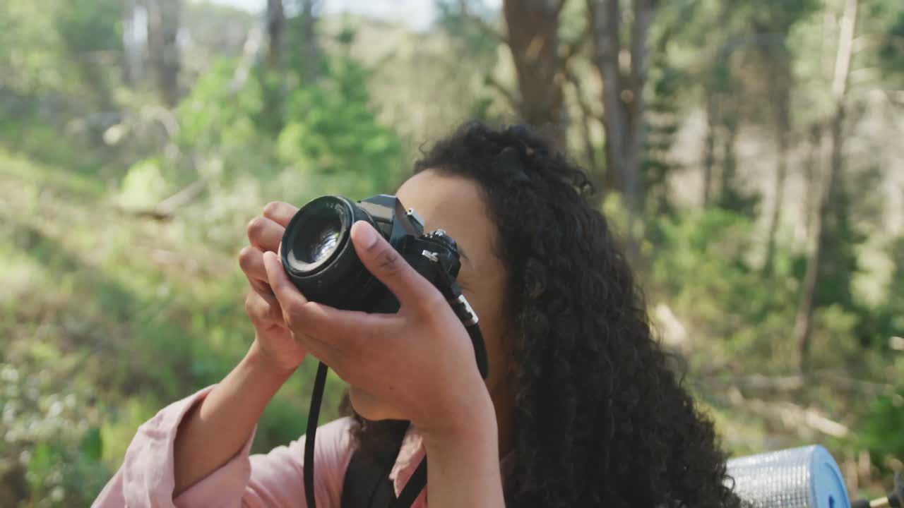 mujer biracial sonriente tomando una foto en el bosque durante una caminata en el campo