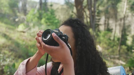 Smiling-biracial-woman-taking-photo-in-forest-during-hiking-in-countryside