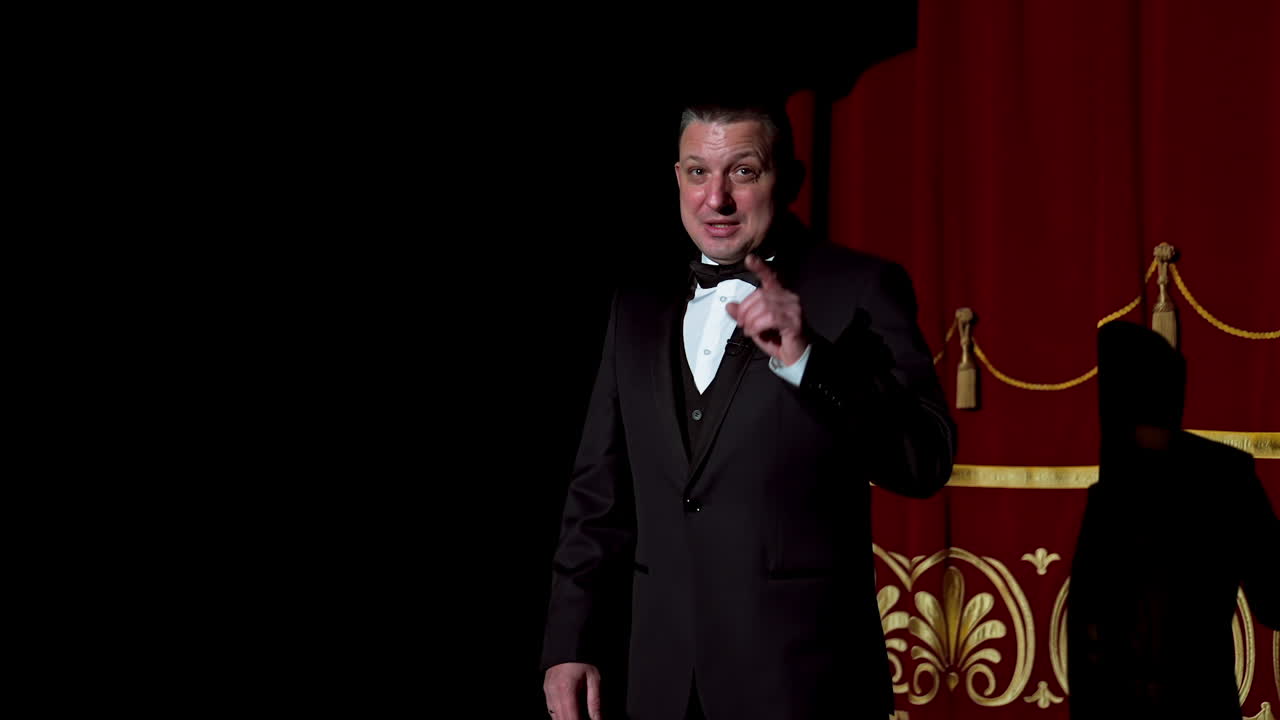 Announcer on a stage in theater. Bright round light on one person. Man in black suit performs to the auditorium.
