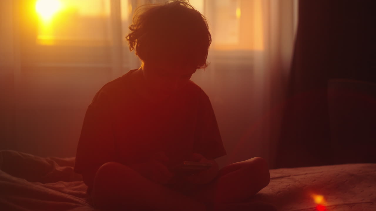 Child Sitting in Bedroom at Sunset with Phone
