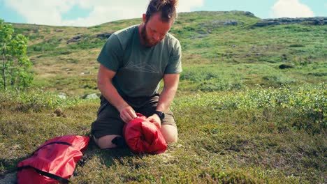 a man packing up the tent he used for camping on rugged terrain between imefjelsvatnet and gurben in indre fosen, trøndelag, norway - static shot