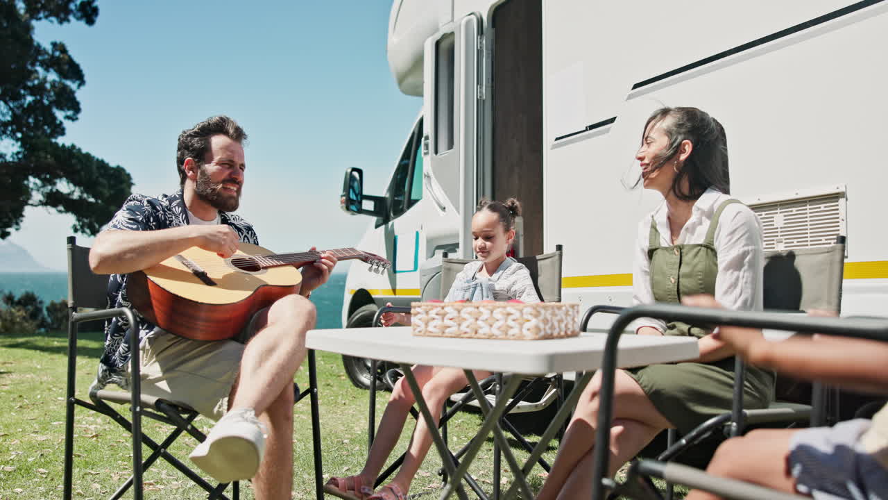 Glückliche Familie spielt Gitarre und entspannt am Wohnmobil an sonniger Küste