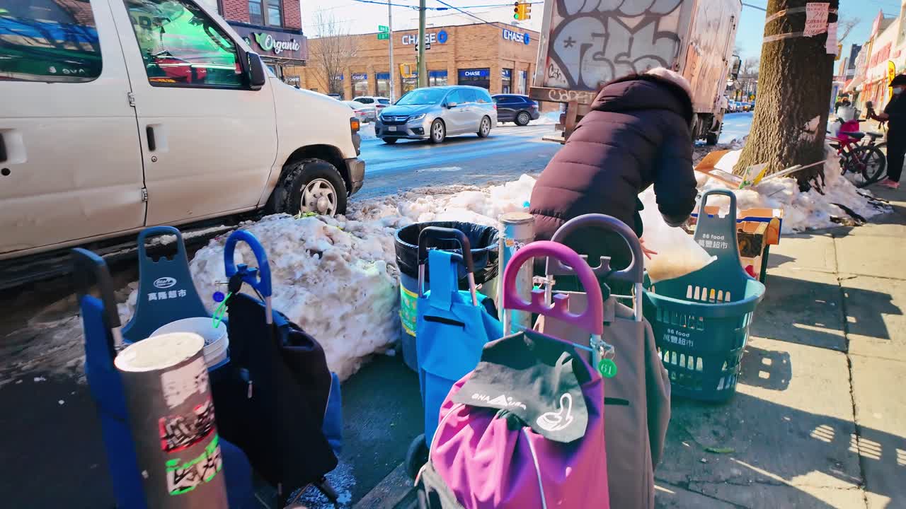 2025年12月2日、米国ニューヨーク：雪の降るニューヨークの歩道に駐車された個人のショッピングカートの列。賑やかな都会の通りで、雪山の近くに並べられた複数のカラフルな折りたたみ式食料品用トロリー。