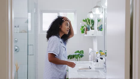 mujer con pijama de pie frente al espejo del baño poniendo maquillaje