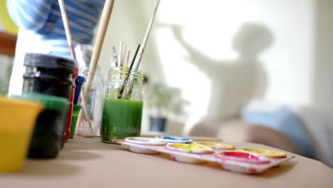 senior biracial woman wearing apron and painting at home