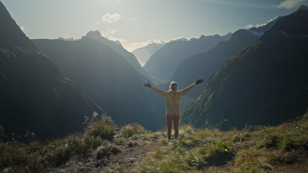 mujer alegre poniendo las manos en el aire mientras mira la hermosa vista de la montaña